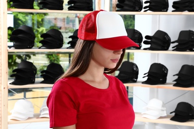 Young woman in blank colorful cap at store. Mock up for design