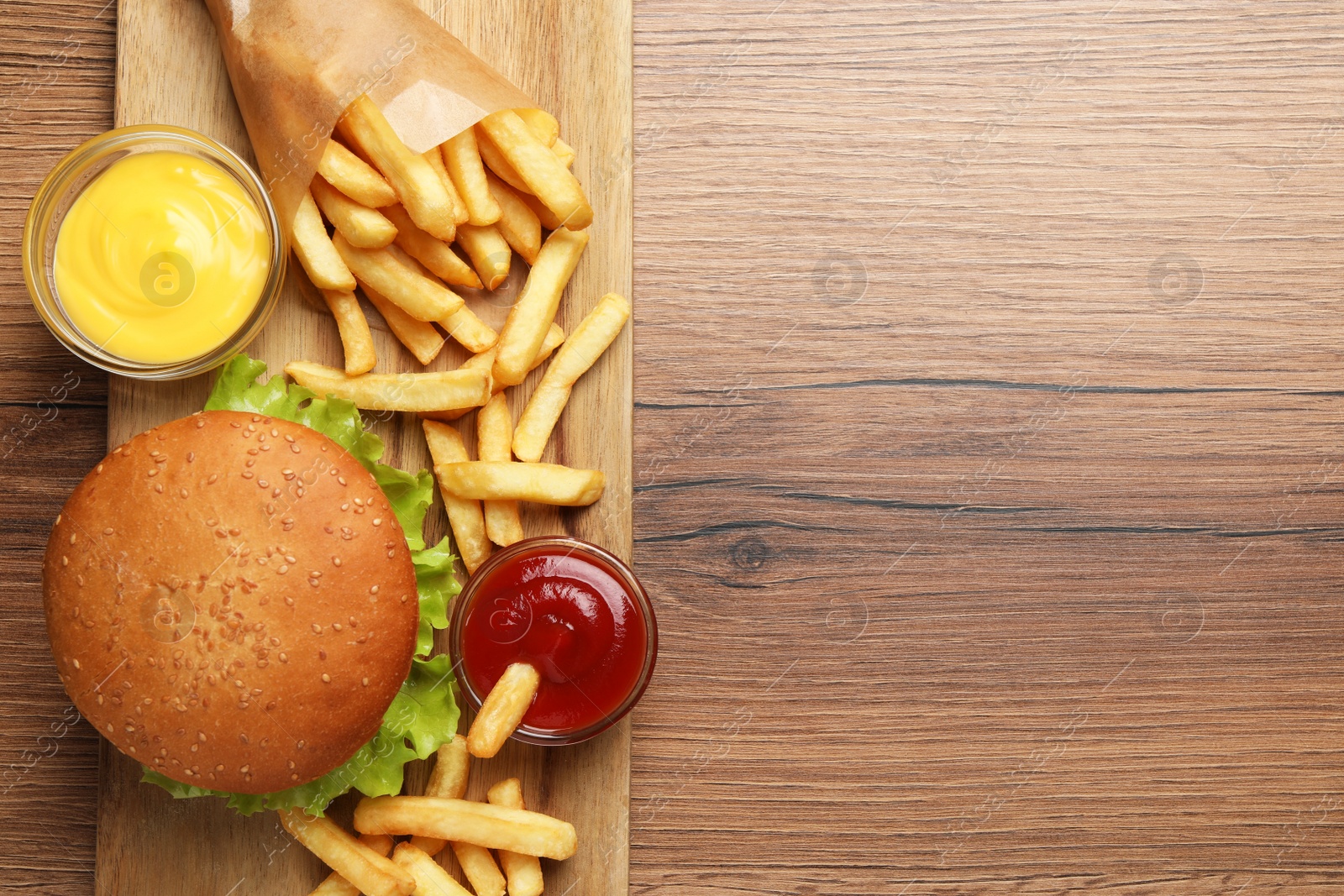 Photo of French fries, tasty burger and sauces on wooden table, top view. Space for text