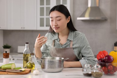 Beautiful woman smelling soup after cooking at countertop in kitchen