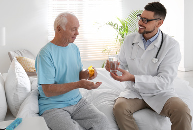 Photo of Doctor giving water to senior patient with pills in modern hospital