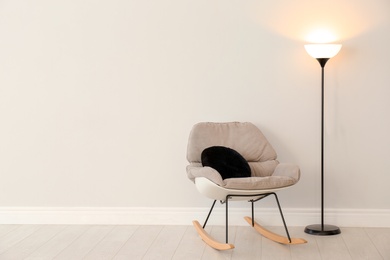 Photo of Modern floor lamp and rocking chair against light wall indoors. Space for text