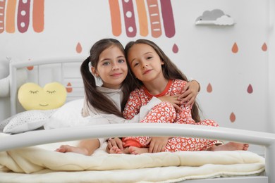 Photo of Cute girls in pajamas on bed at home