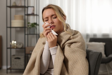 Photo of Sick woman wrapped in blanket with tissue in armchair at home. Cold symptoms