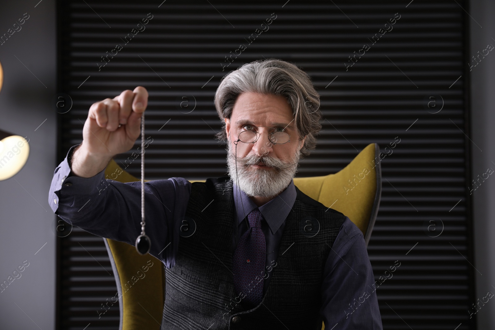 Photo of Psychotherapist with pendulum in office. Hypnotherapy session