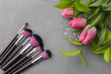 Makeup brushes and flowers on grey background