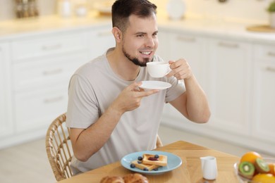 Smiling man drinking coffee at breakfast indoors