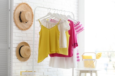 Photo of Wardrobe rack with women's clothes at white brick wall in room