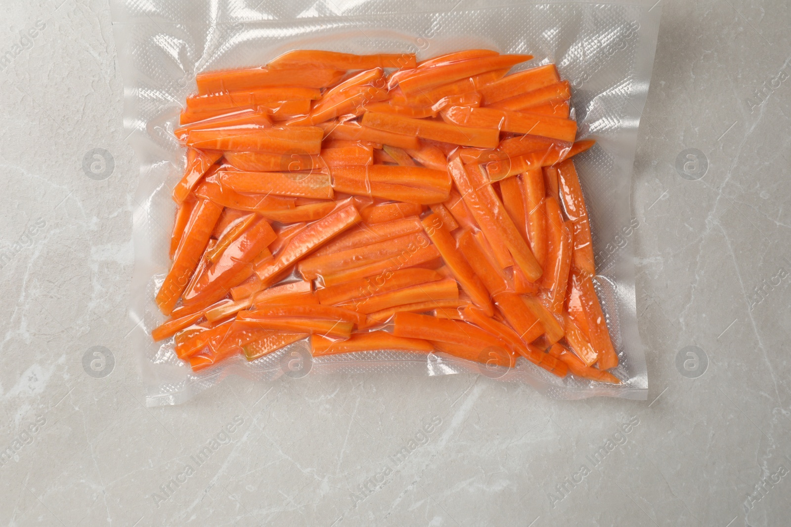 Photo of Vacuum packing with cut carrots on light grey marble table, top view