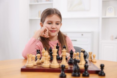 Cute girl playing chess at table in room