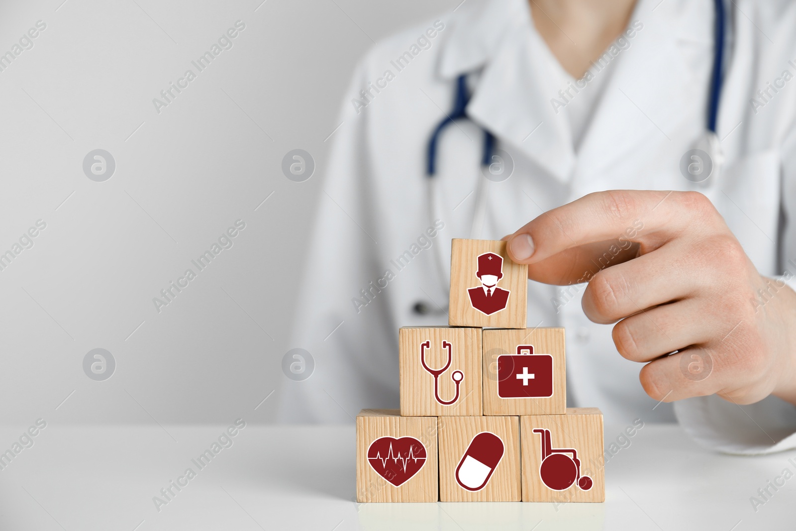 Image of Doctor building pyramid of wooden cubes with different icons at white table, closeup. Insurance concept