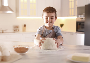 Photo of Cute little boy with dough at table in kitchen. Cooking pastry
