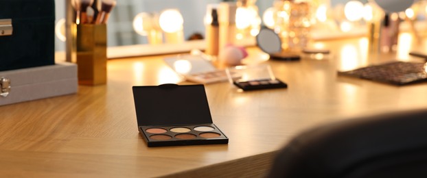 Image of Makeup room. Eyeshadow palette and other cosmetic products on wooden dressing table indoors, banner design