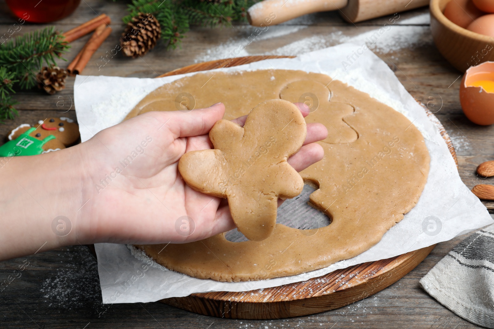 Photo of Making homemade Christmas cookies. Woman holding gingerbread man above wooden table, closeup