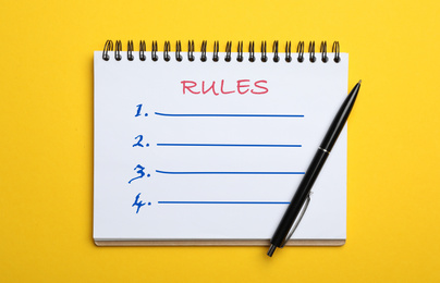 Image of Notebook with list of rules and pen on yellow background, top view