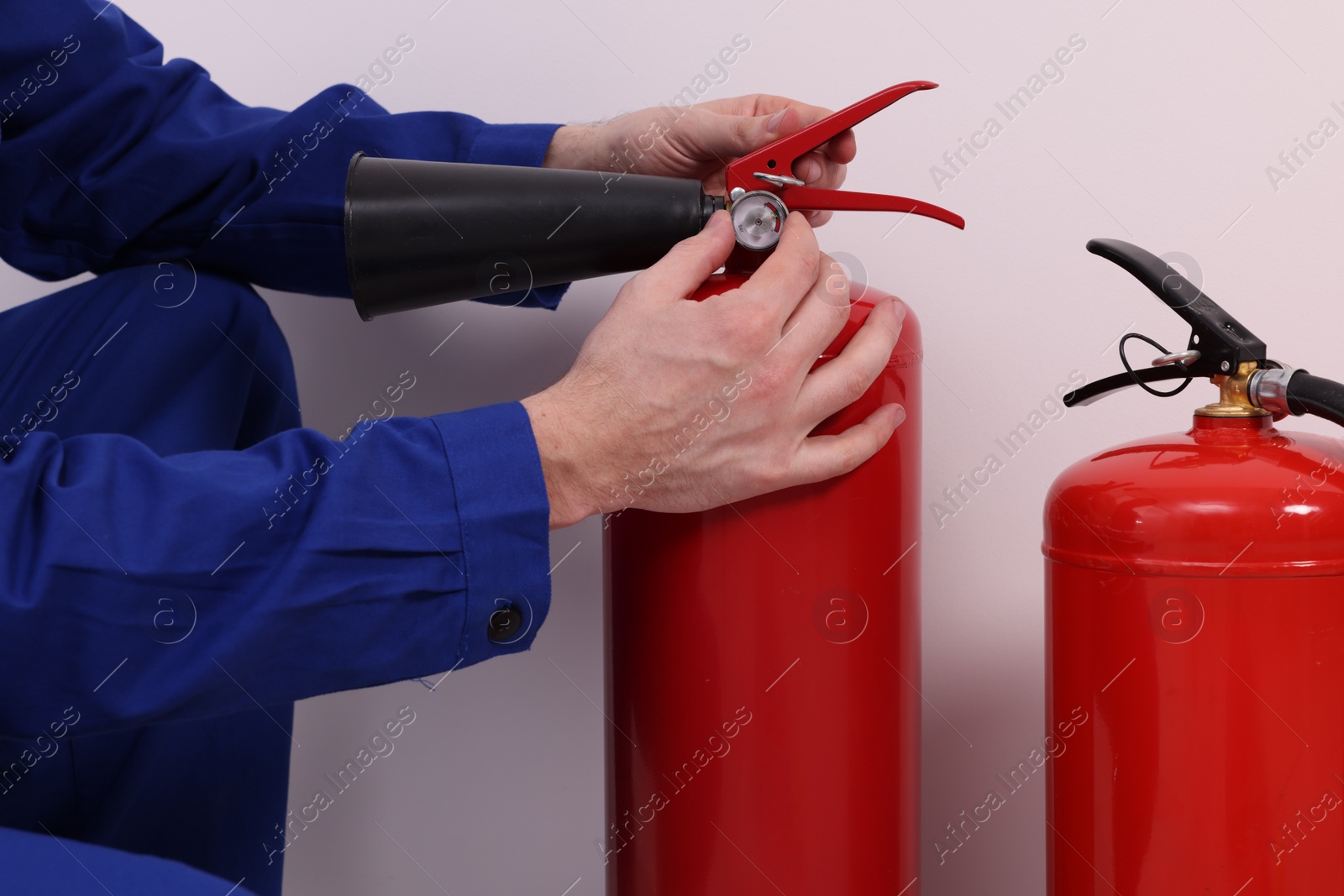 Photo of Man checking quality of fire extinguishers indoors, closeup