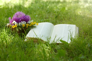 Photo of Open book and beautiful wildflowers on green grass outdoors