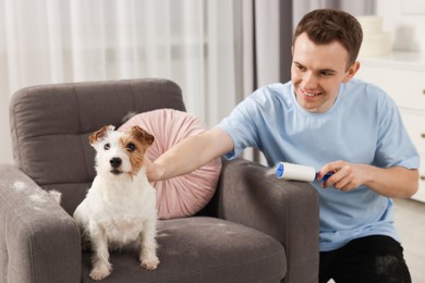 Photo of Smiling man removing pet's hair from armchair at home