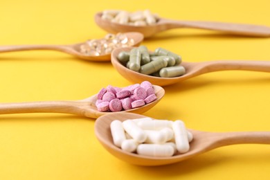 Different vitamin pills in wooden spoons on yellow background, closeup