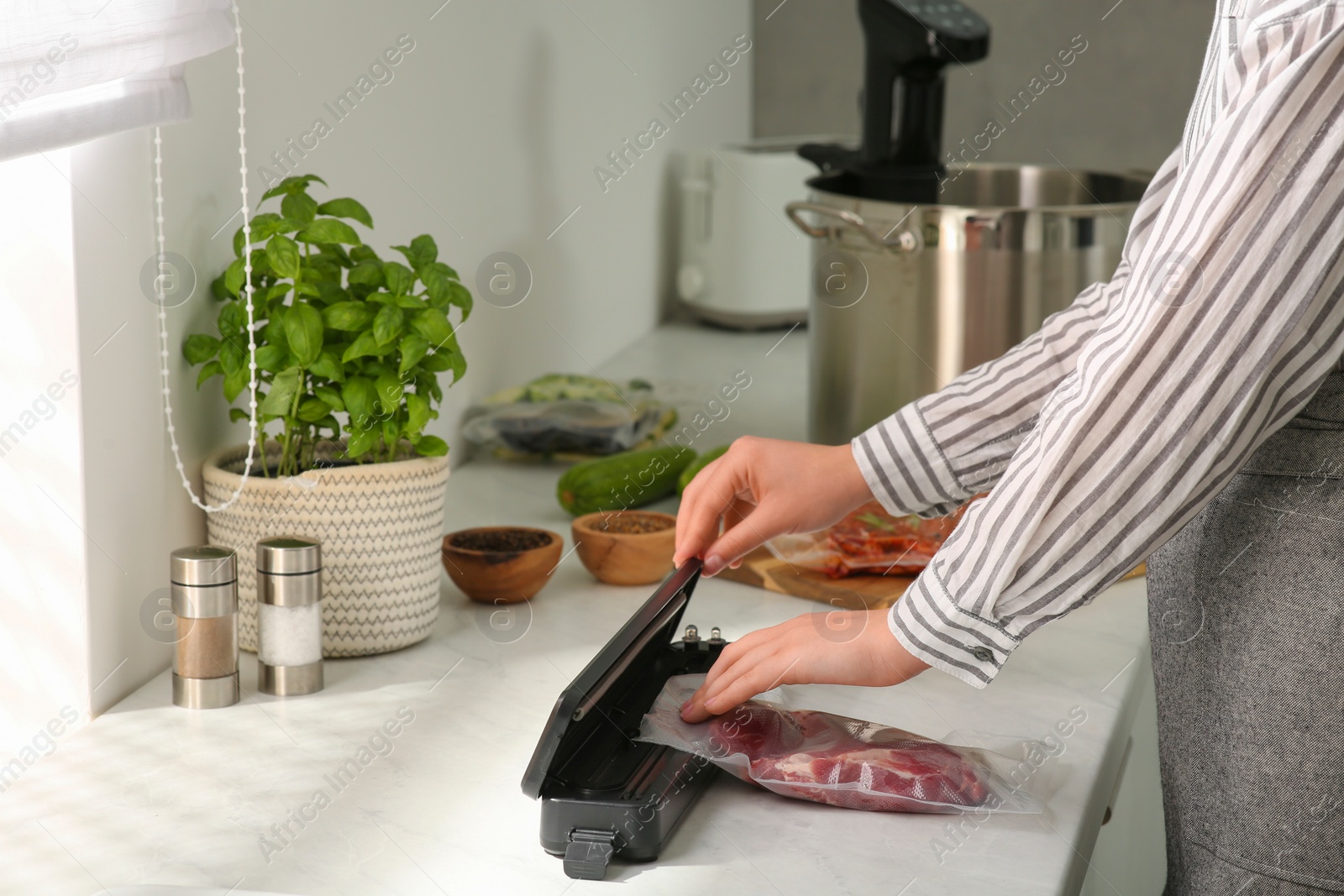 Photo of Woman using sealer for vacuum packing in kitchen, closeup. Sous vide cooking