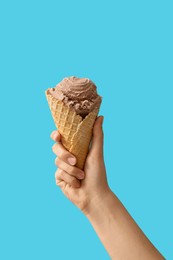 Woman holding waffle cone with delicious chocolate ice cream on light blue background, closeup