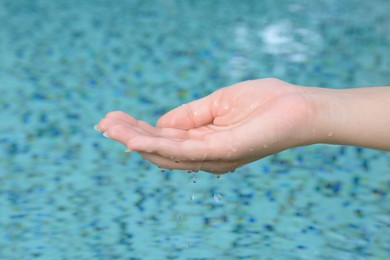 Photo of Girl holding water in hand above pool, closeup