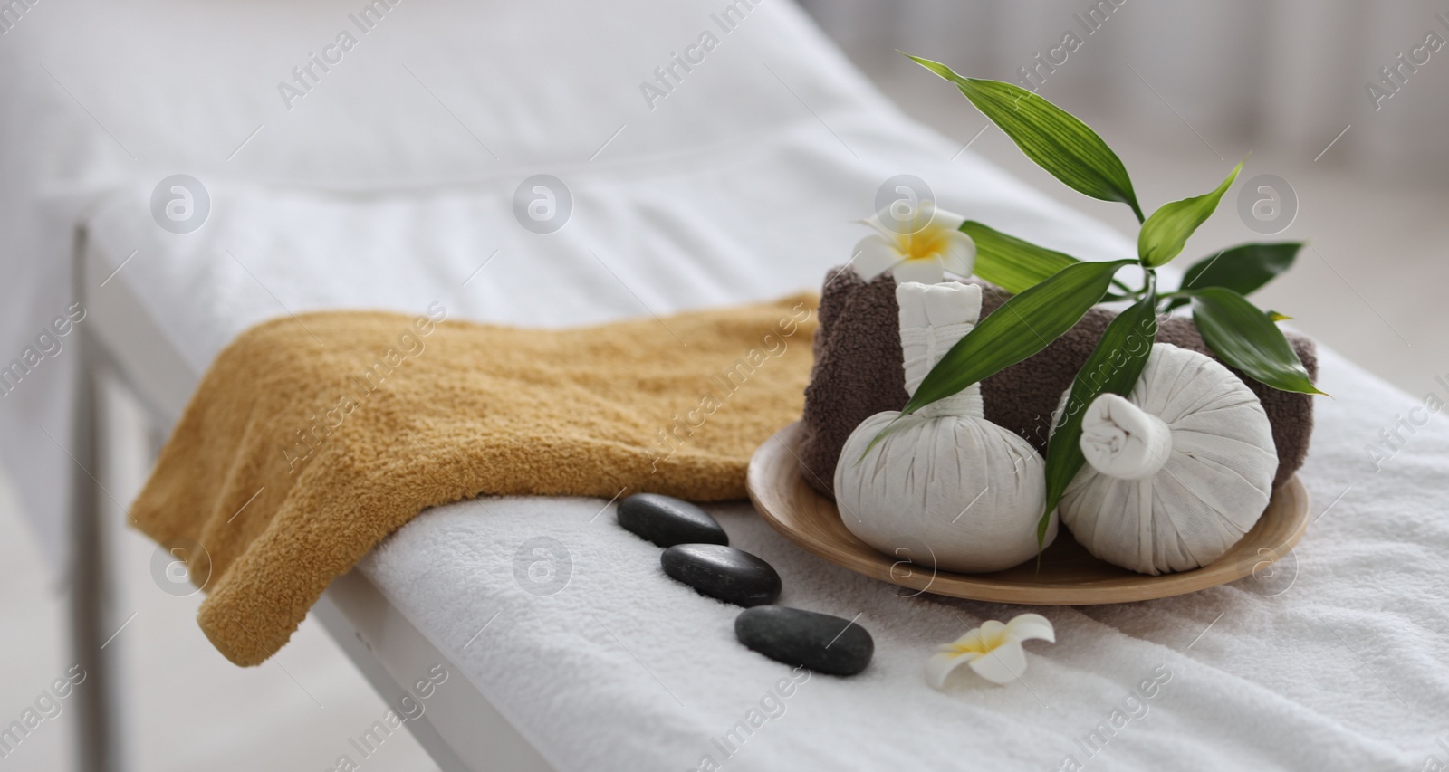 Photo of Spa stones, flowers, towel and herbal bags on massage table indoors