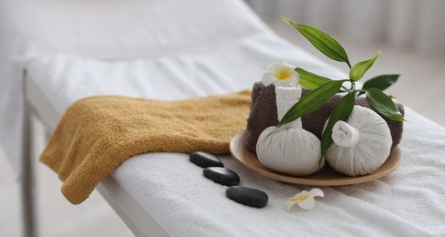 Photo of Spa stones, flowers, towel and herbal bags on massage table indoors