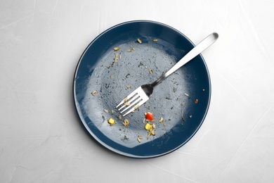 Photo of Dirty plate with food leftovers and fork on grey background, top view