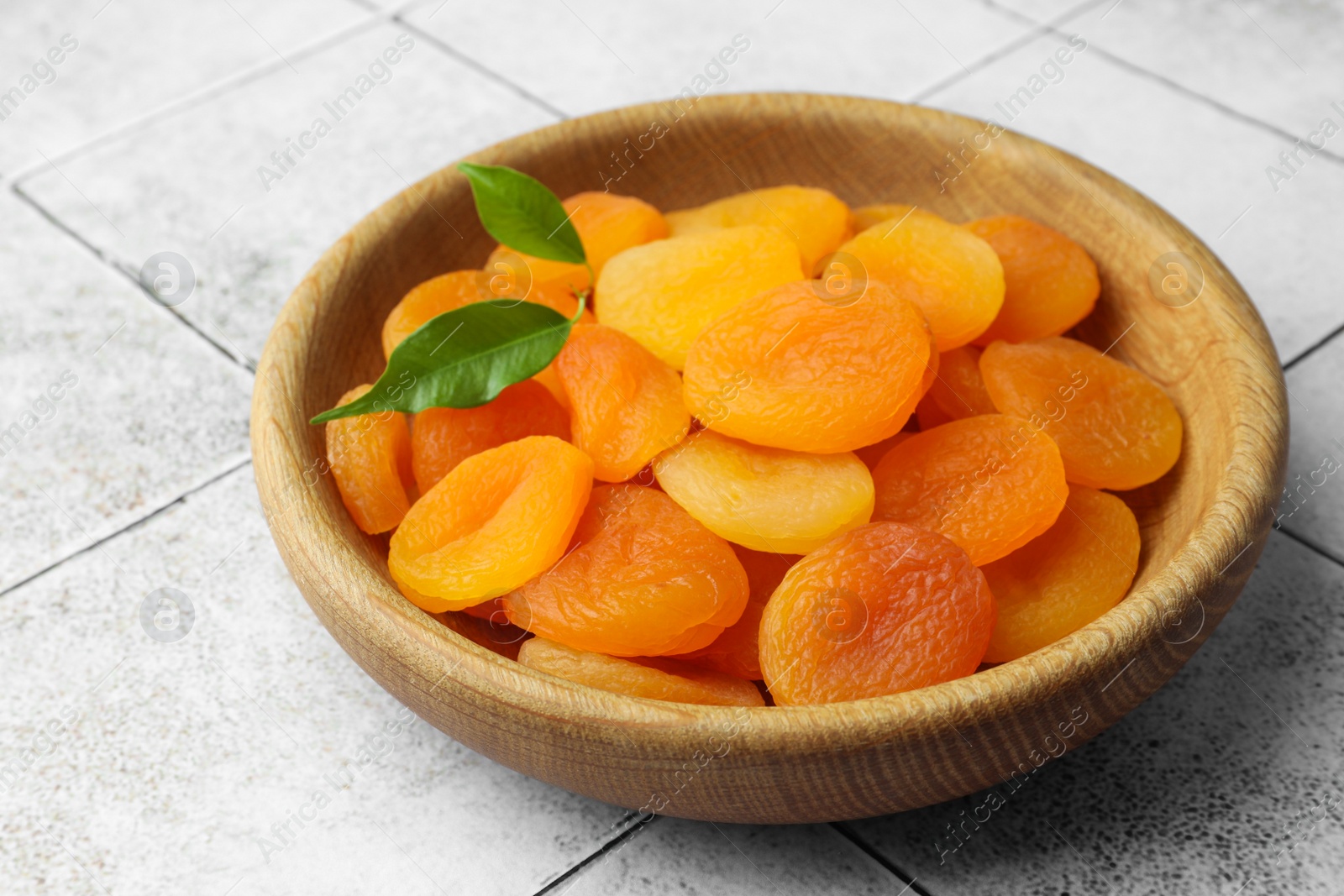 Photo of Wooden bowl of tasty apricots on white tiled table. Dried fruits