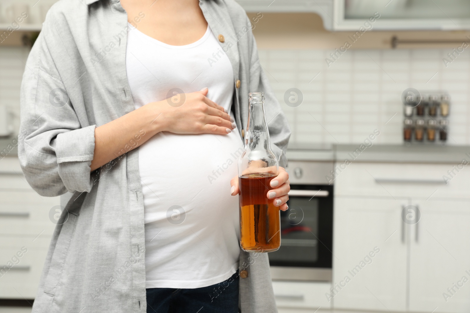 Photo of Future mother with bottle of alcohol drink in kitchen, closeup. Bad habits during pregnancy