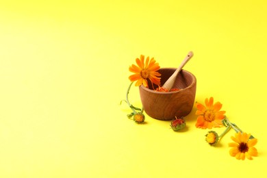 Mortar with pestle and beautiful calendula flowers on yellow background, space for text