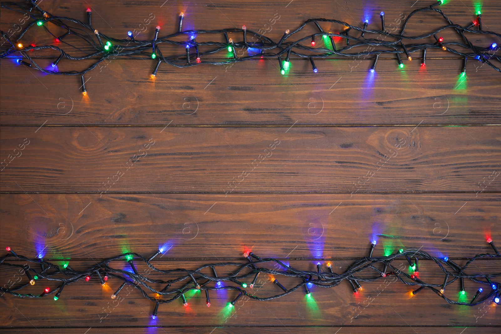 Photo of Glowing Christmas lights on wooden background, top view