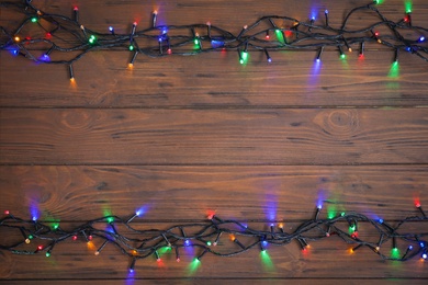 Photo of Glowing Christmas lights on wooden background, top view