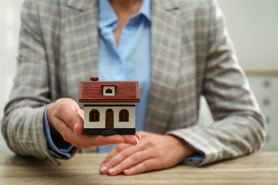 Photo of Real estate agent holding house model at wooden table, closeup