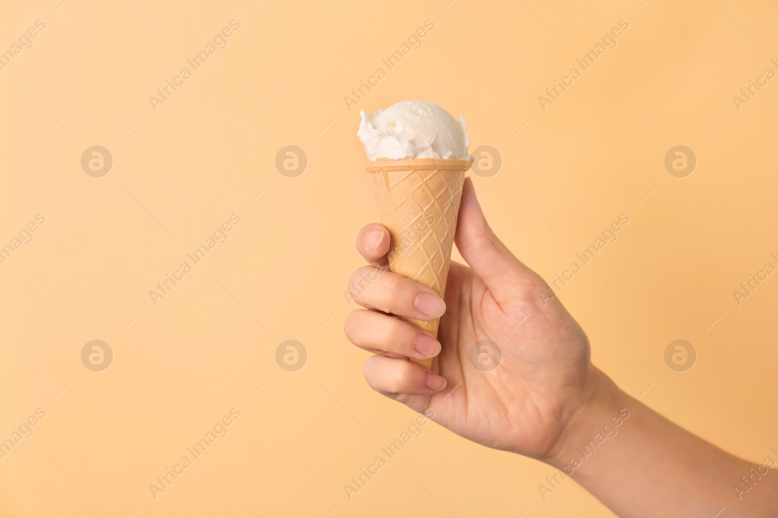 Photo of Woman holding waffle cone with tasty vanilla ice cream on color background