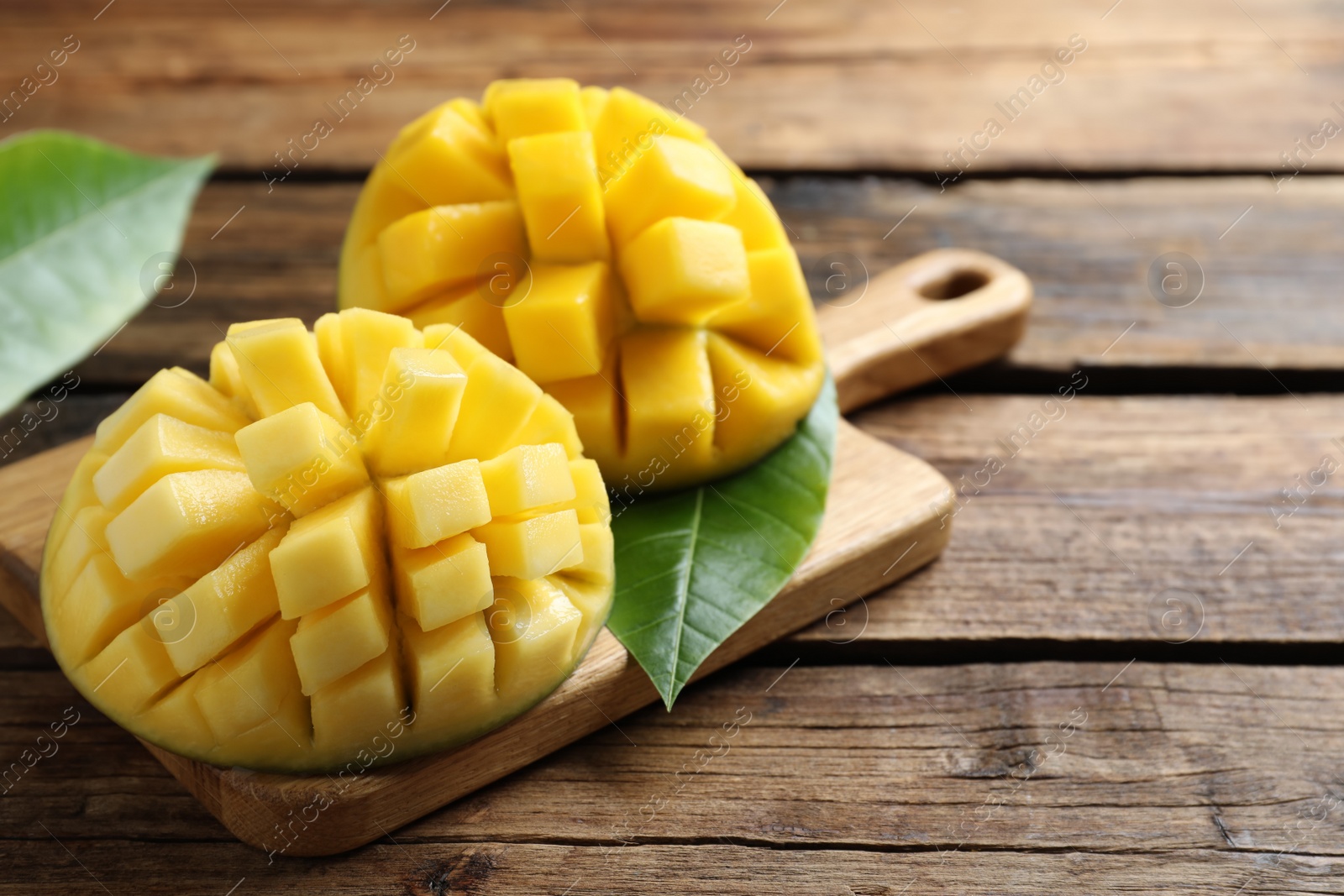 Photo of Halves of ripe mango cut into cubes on wooden table