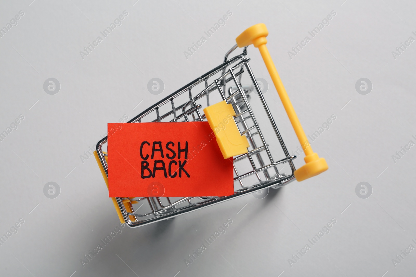 Photo of Card with word Cashback in shopping cart on light grey background, top view