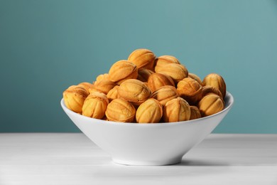 Photo of Freshly baked walnut shaped cookies in bowl on white wooden table against light blue background. Homemade pastry filled with caramelized condensed milk