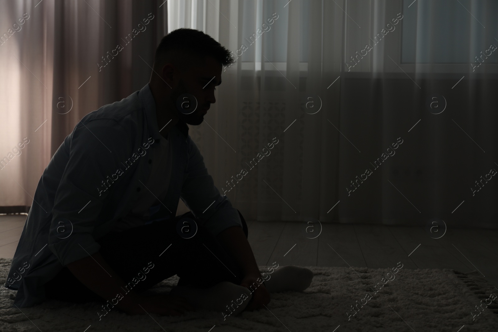 Photo of Silhouette of sad man in dark room. Space for text