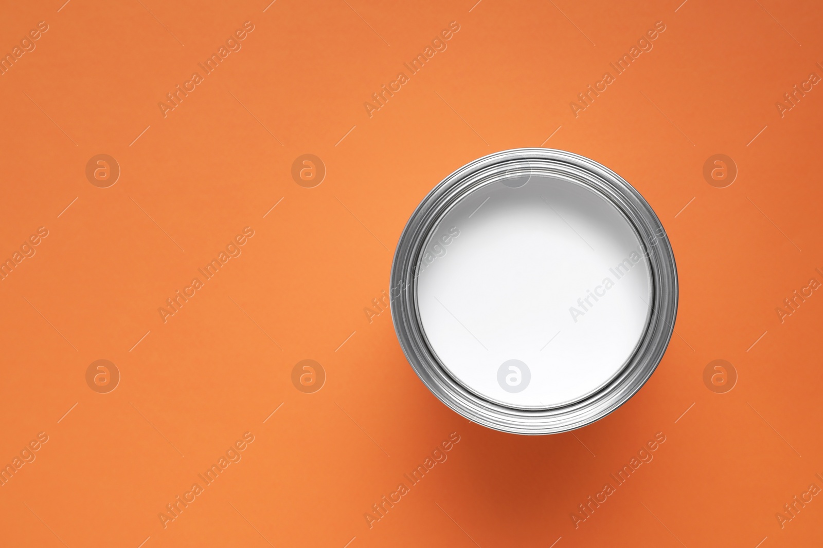 Photo of Can with white paint on orange background, top view. Space for text