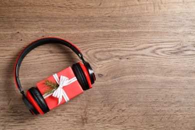 Modern headphones and gift box on wooden background, top view with space for text. Christmas music concept