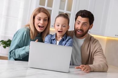 Emotional family with laptop at white table indoors