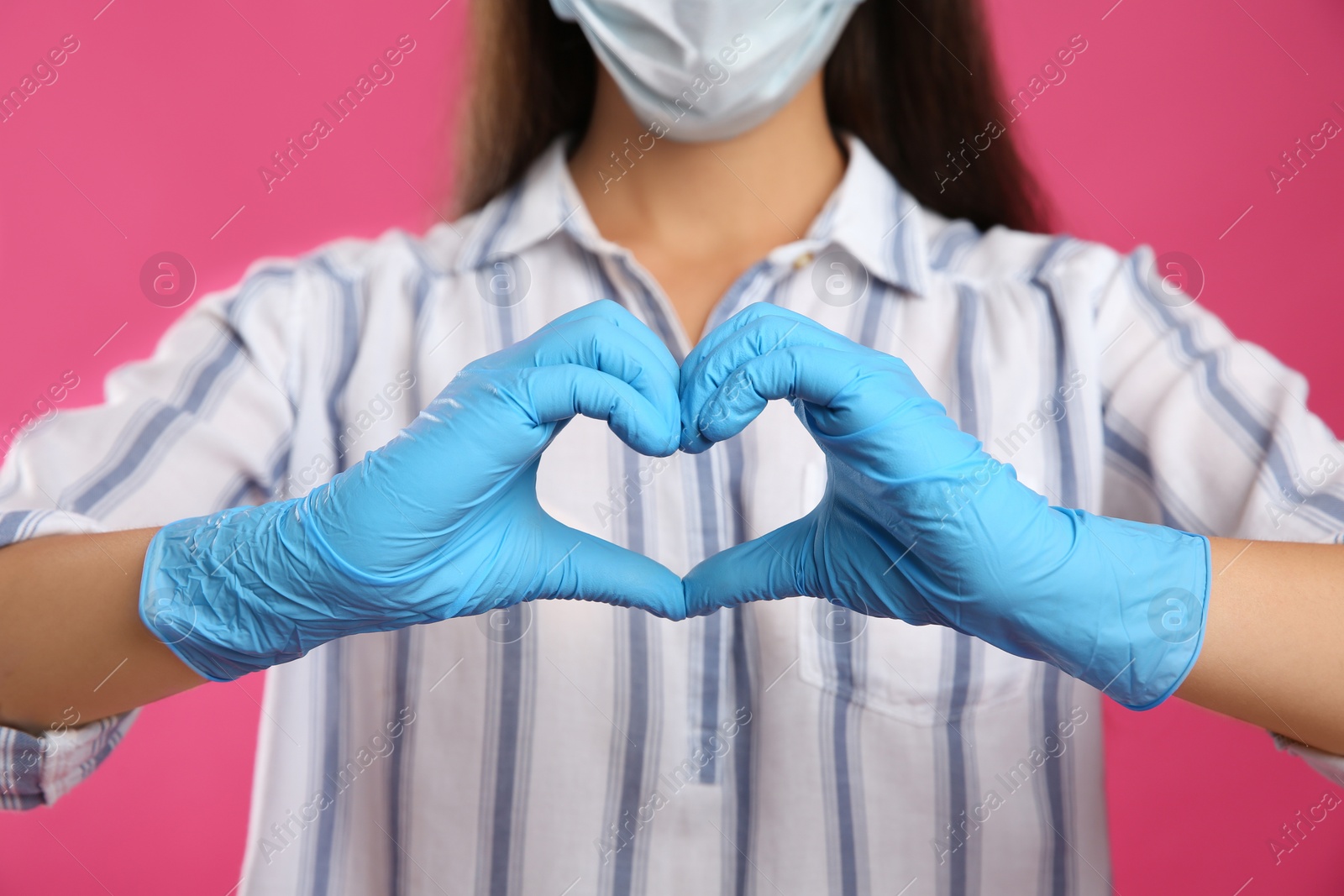 Photo of Woman in protective face mask and medical gloves making heart with hands on pink background, closeup