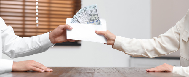 Image of Woman giving bribe money to man at table indoors, closeup. Banner design