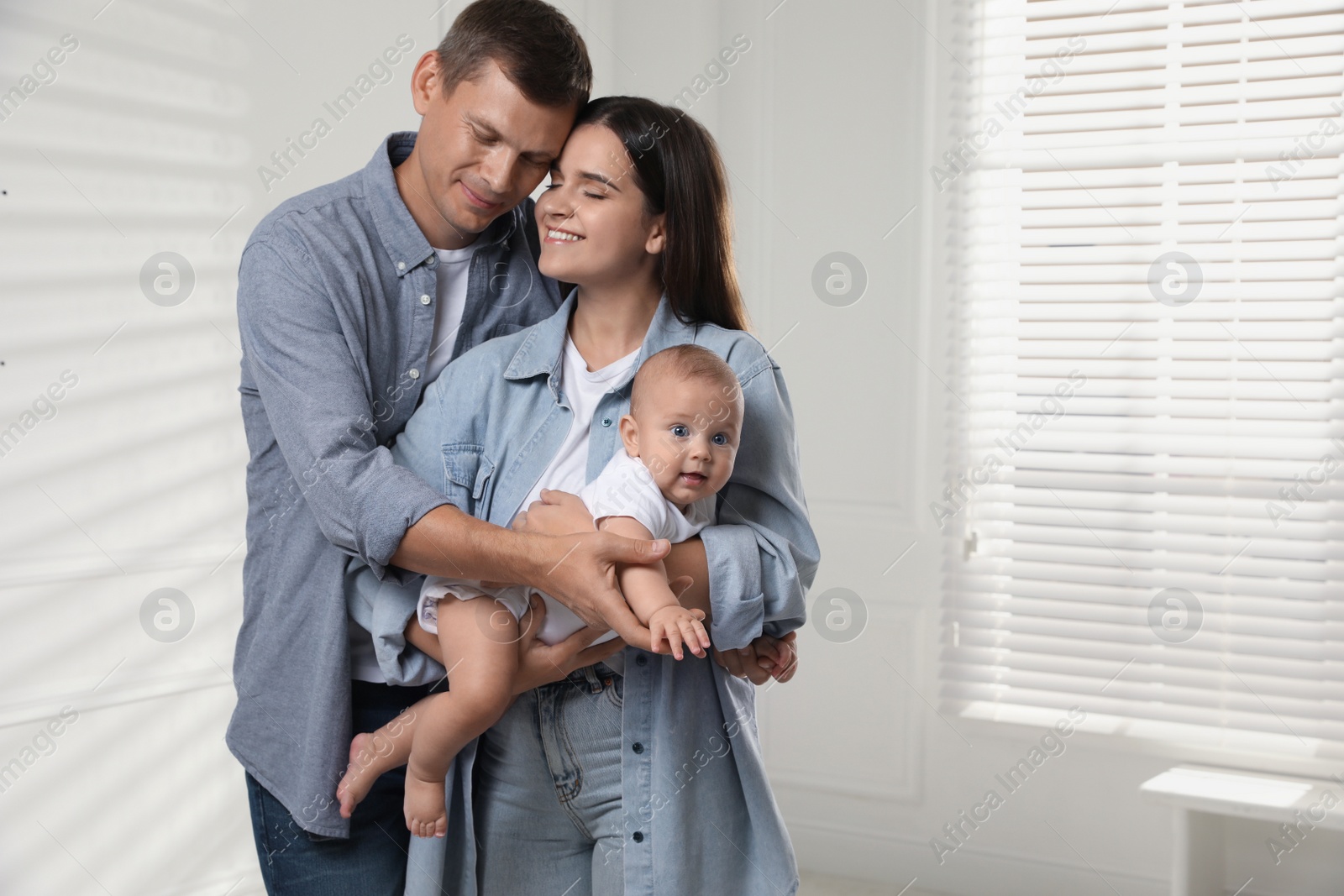 Photo of Happy family. Couple with their cute baby near window indoors, space for text