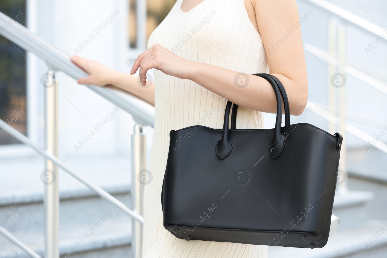 Photo of Young woman with stylish leather bag on stairs outdoors, closeup