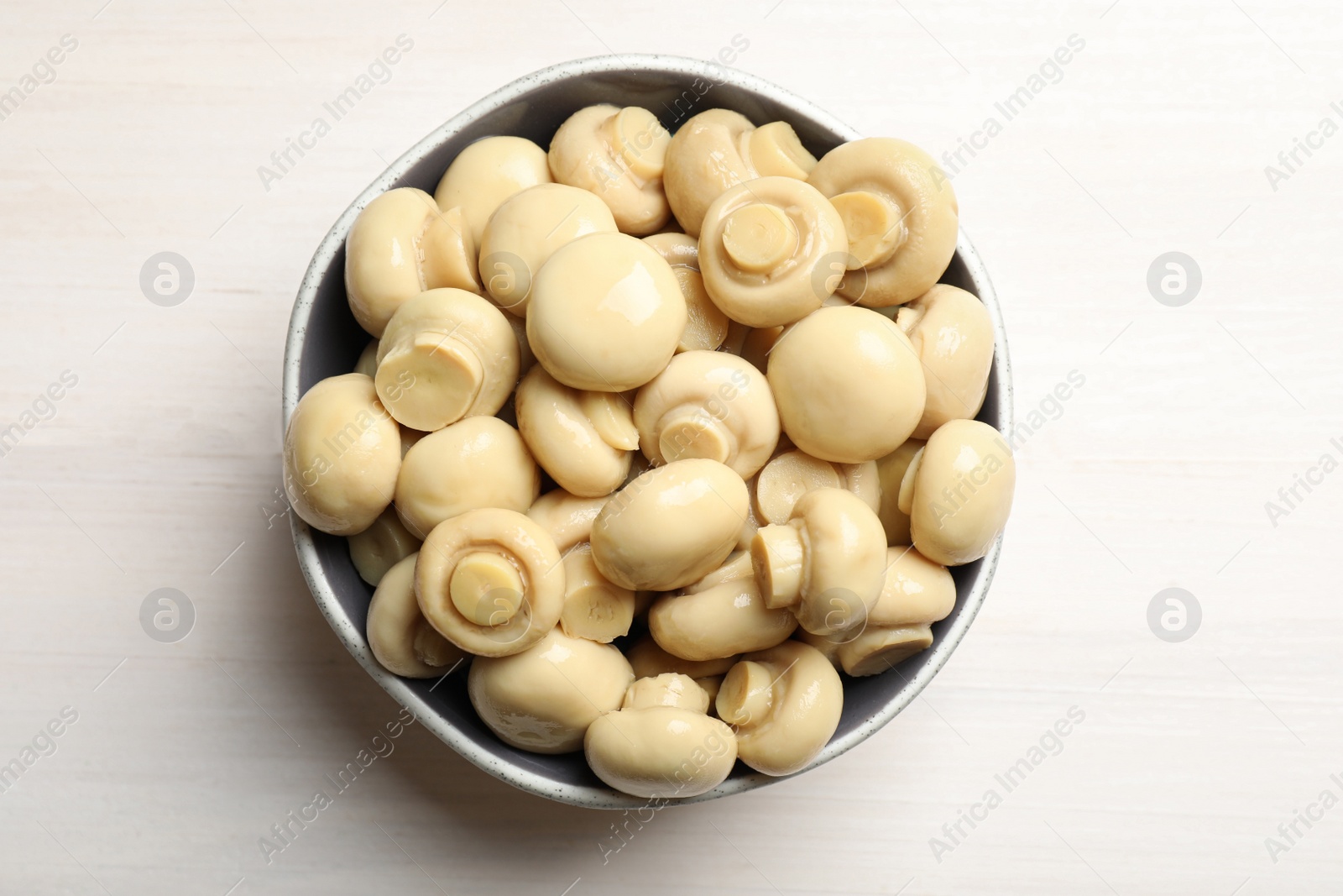 Photo of Delicious marinated mushrooms in bowl on white wooden table, top view