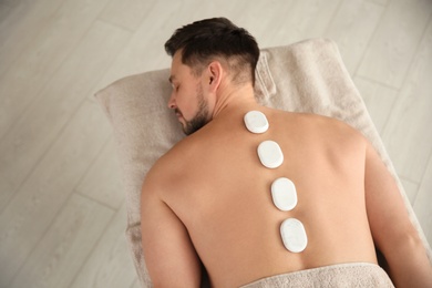 Photo of Handsome man receiving hot stone massage in spa salon, above view. Space for text