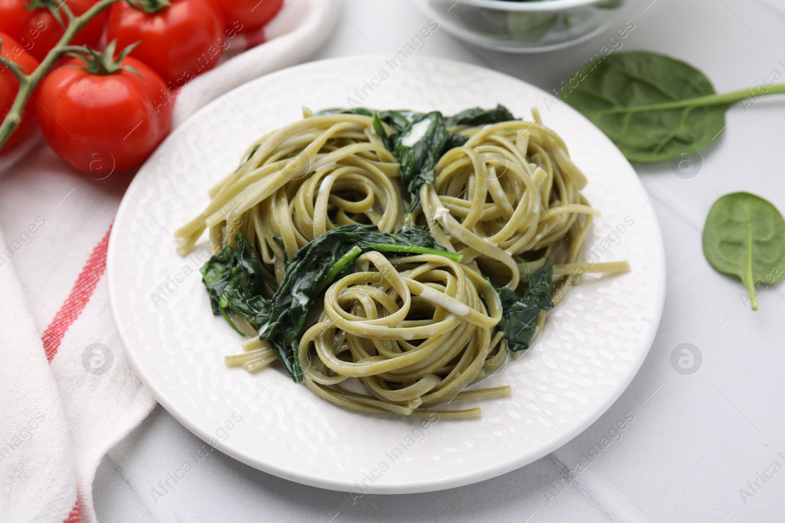 Photo of Tasty pasta with spinach and sauce on white tiled table