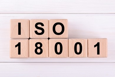 Photo of International Organization for Standardization. Cubes with abbreviation ISO and number 18001 on white wooden table, flat lay